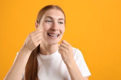 Photo of Girl with braces cleaning teeth with dental floss on orange background