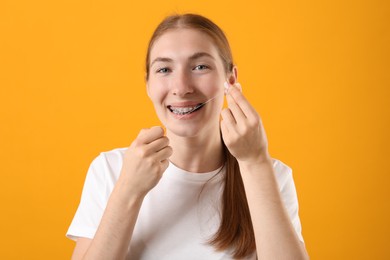 Photo of Girl with braces cleaning teeth with dental floss on orange background