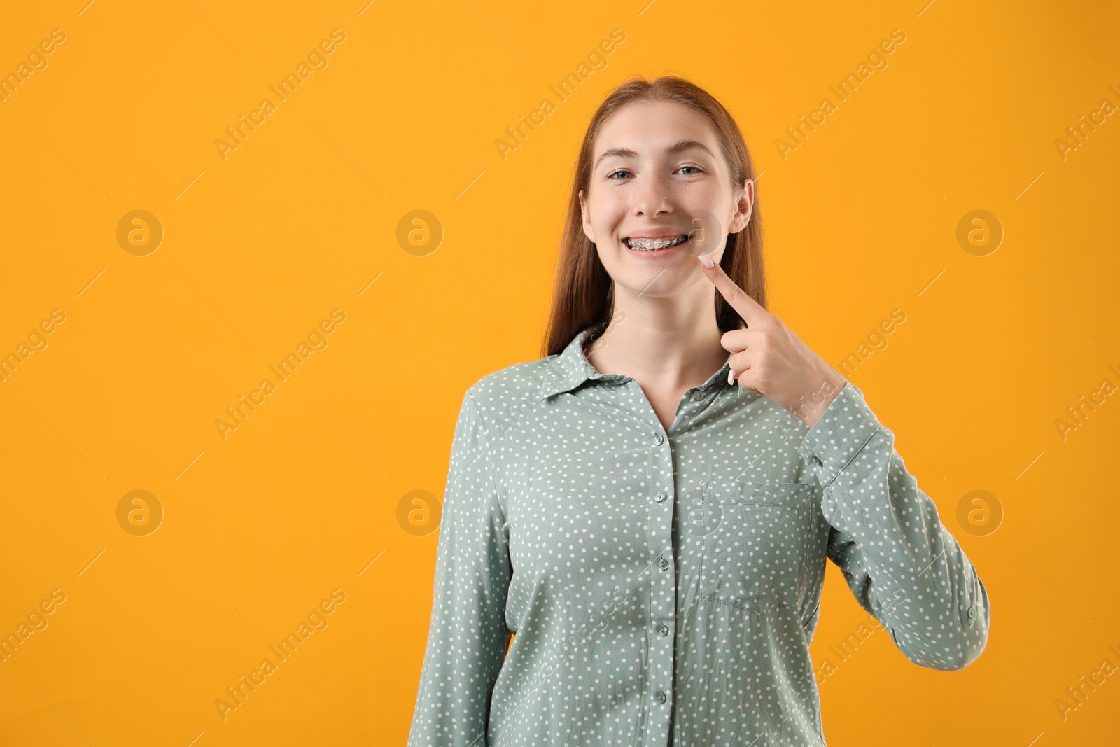 Photo of Girl pointing at her braces on orange background, space for text