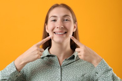 Photo of Girl pointing at her braces on orange background