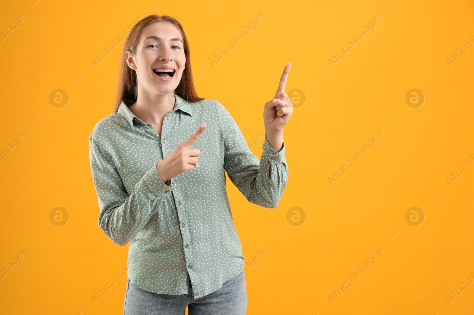 Photo of Smiling girl with braces on orange background, space for text