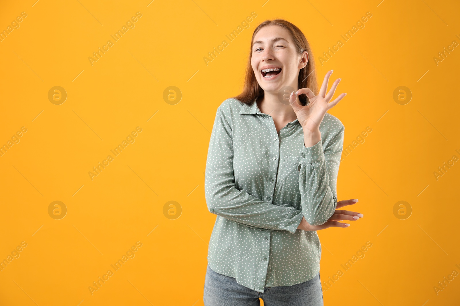 Photo of Smiling girl with braces showing ok gesture on orange background, space for text