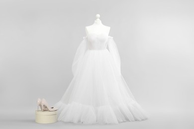 Photo of Mannequin with beautiful wedding dress and shoes on light grey background