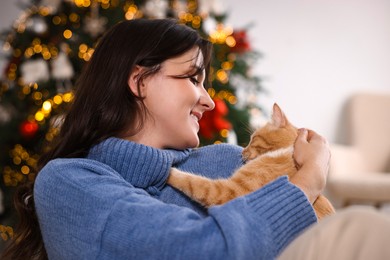 Photo of Woman with cute ginger cat in room decorated for Christmas