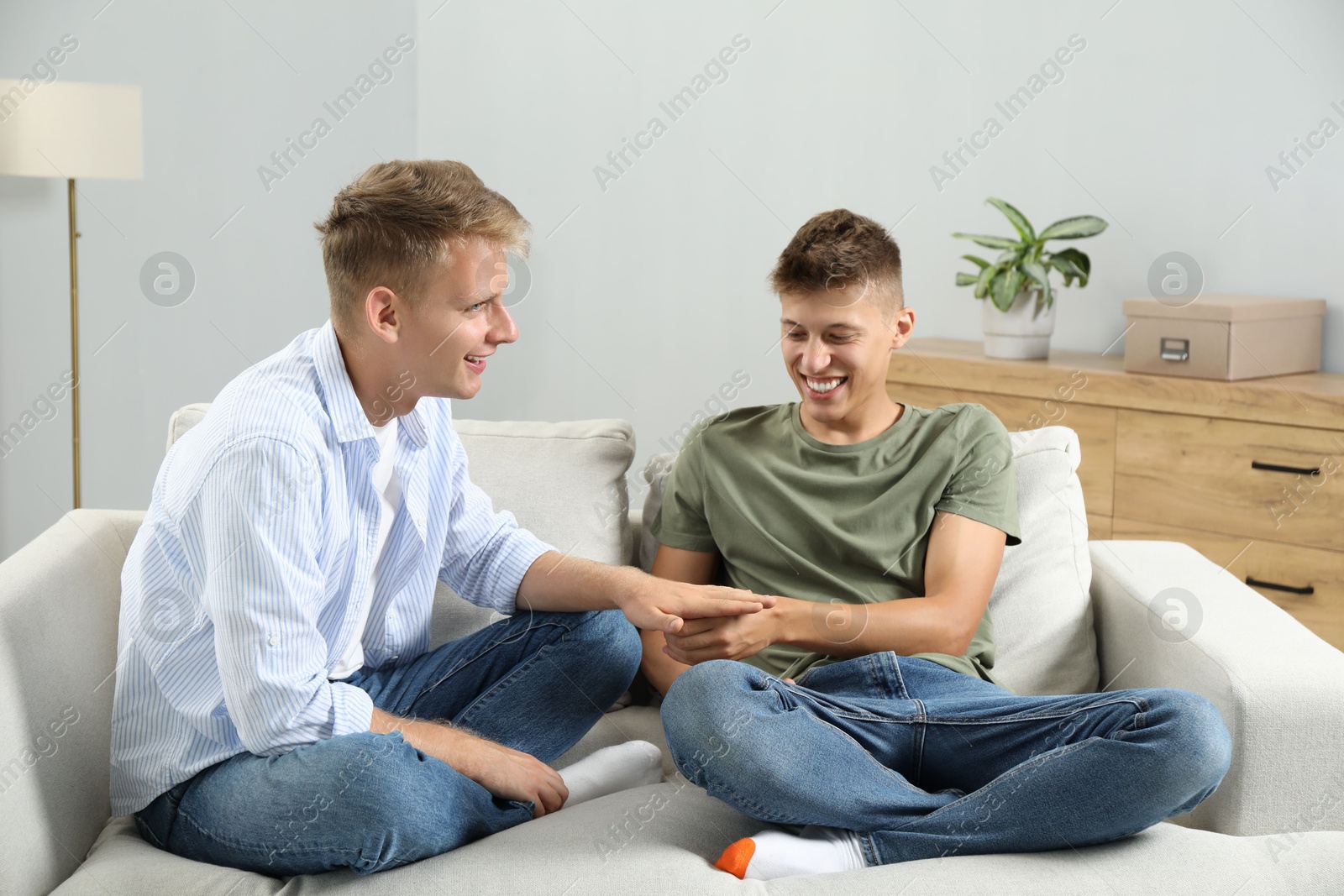 Photo of Happy brothers playing rock, paper and scissors on sofa at home