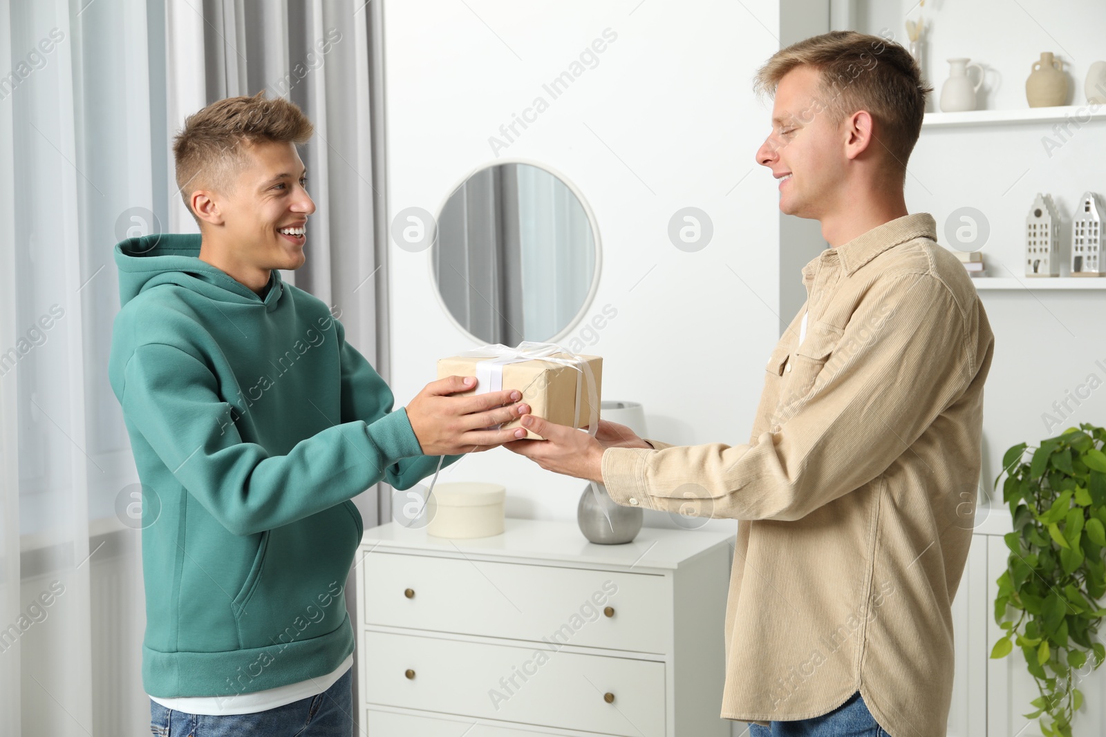 Photo of Happy man presenting gift to his brother at home