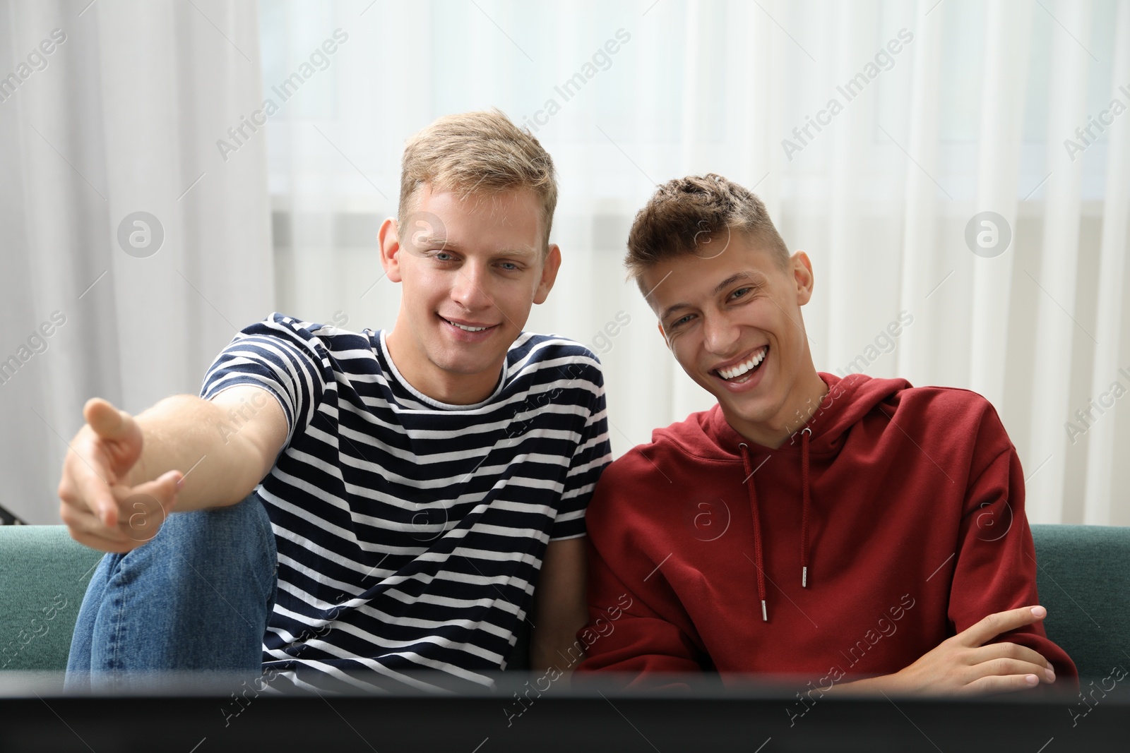 Photo of Young brothers watching tv on sofa at home