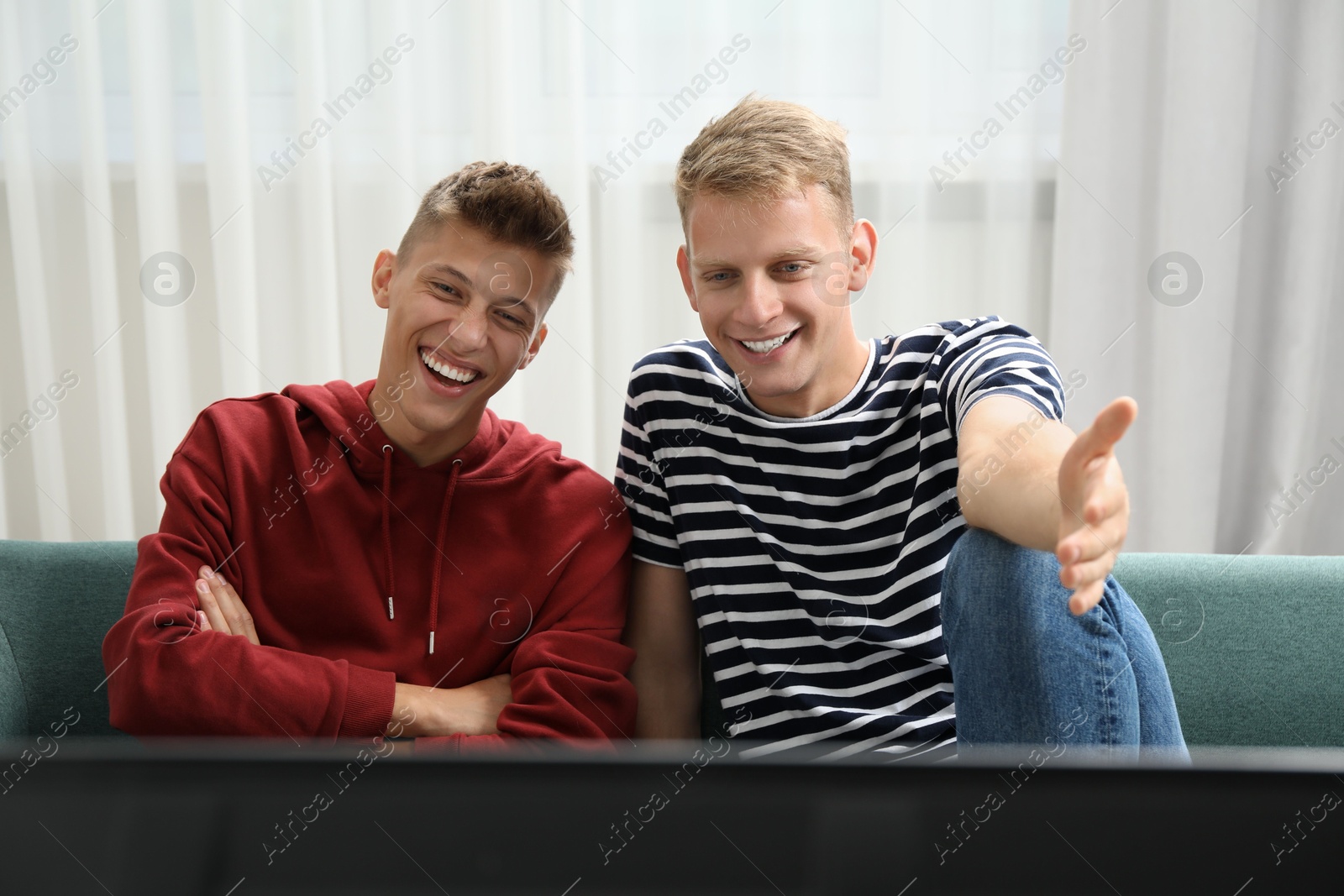 Photo of Young brothers watching tv on sofa at home