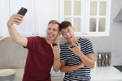 Photo of Young brothers taking selfie and showing rock gesture in kitchen