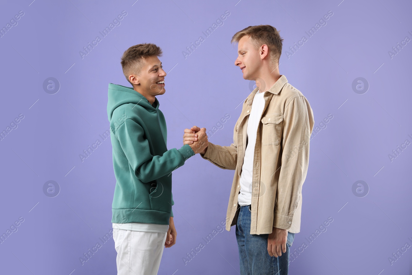 Photo of Happy brothers clasping hands on violet background