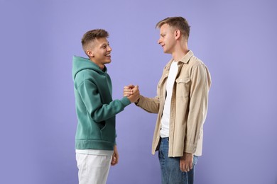 Photo of Happy brothers clasping hands on violet background