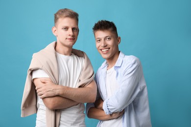 Happy brothers posing with crossed arms on light blue background