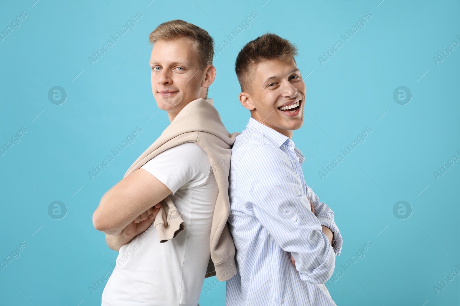 Photo of Happy brothers posing with crossed arms on light blue background