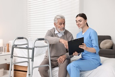 Photo of Doctor consulting senior patient with walking frame in hospital ward