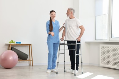 Nurse helping senior man with walking frame in clinic