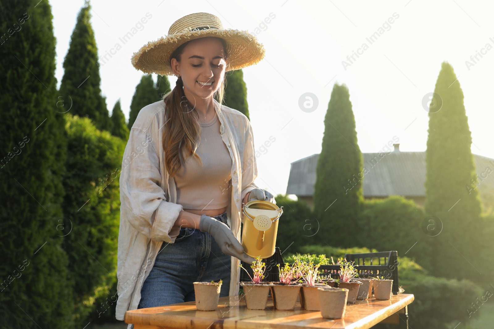 Photo of Smiling woman watering potted seedlings with can at table outdoors