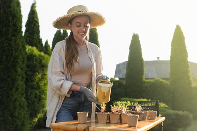 Photo of Smiling woman watering potted seedlings with can at table outdoors