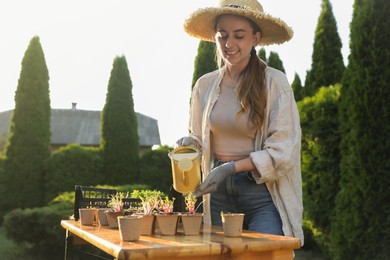 Smiling woman watering potted seedlings with can at table outdoors