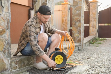 Man with extension cord reel in backyard, space for text