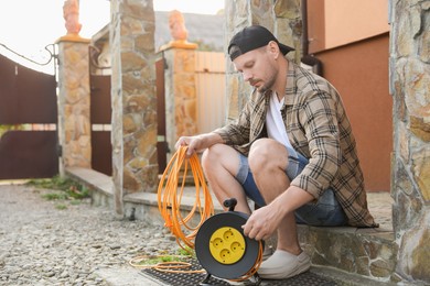 Man with extension cord reel in backyard, space for text