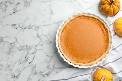 Tasty homemade pumpkin pie and fresh pumpkins on white marble table, top view. Space for text