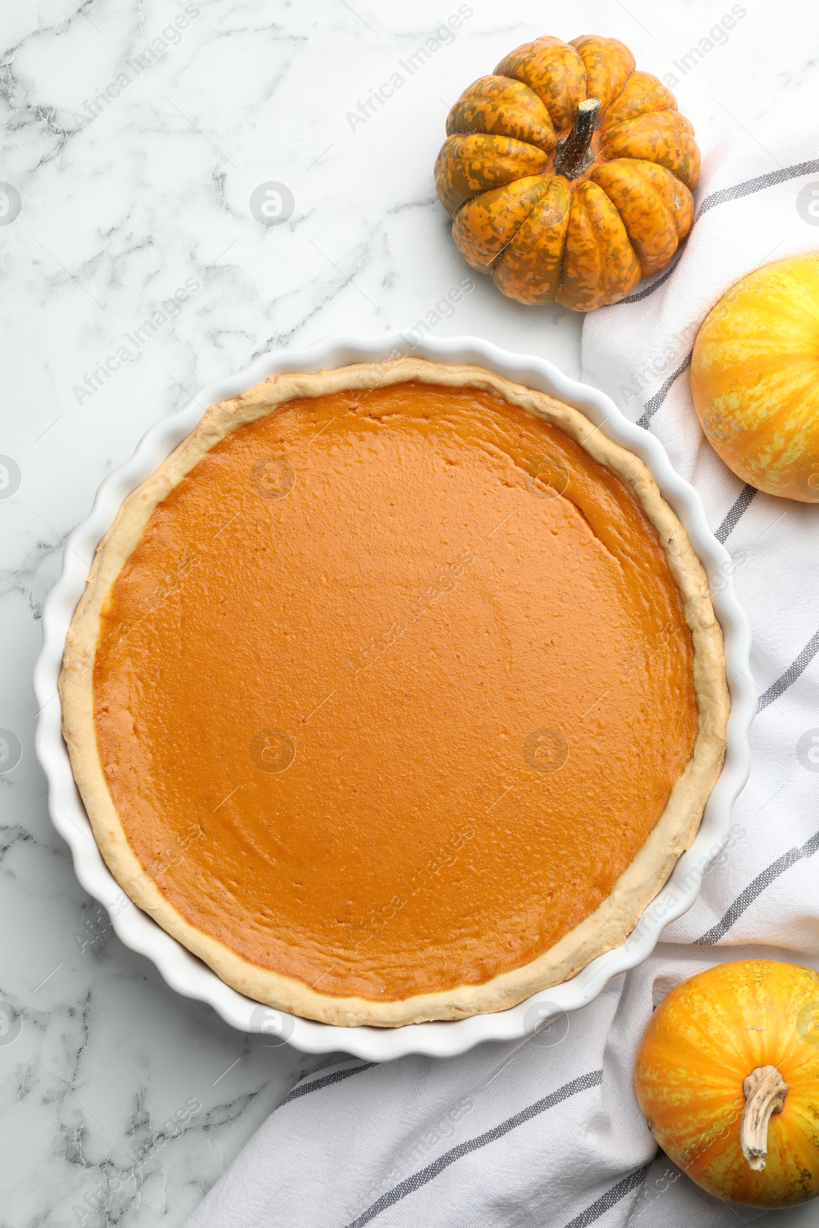 Photo of Tasty homemade pumpkin pie and fresh pumpkins on white marble table, top view