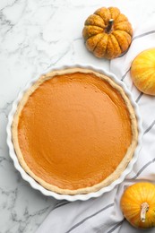 Photo of Tasty homemade pumpkin pie and fresh pumpkins on white marble table, top view