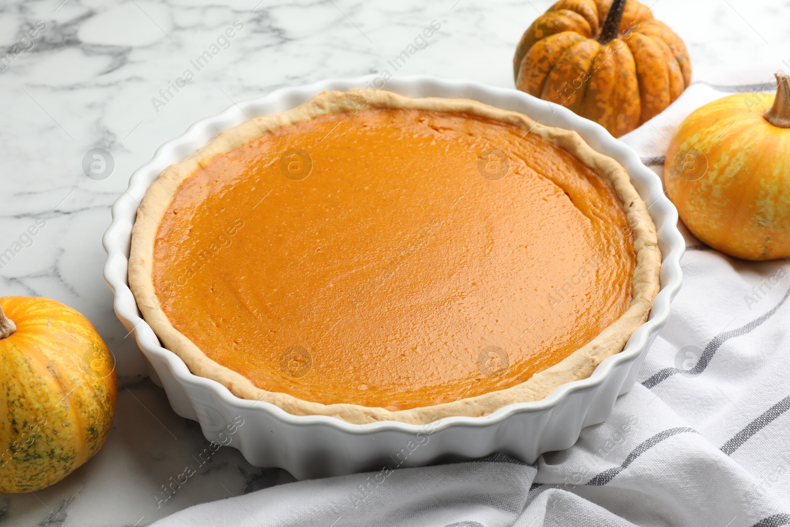 Photo of Tasty homemade pumpkin pie and fresh pumpkins on white marble table, closeup