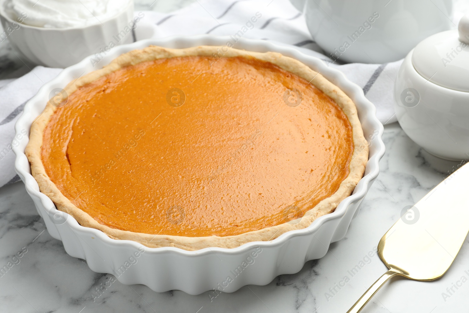 Photo of Tasty homemade pumpkin pie and server on white marble table, closeup