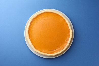 Photo of Tasty homemade pumpkin pie on blue background, top view