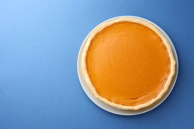 Tasty homemade pumpkin pie on blue background, top view. Space for text