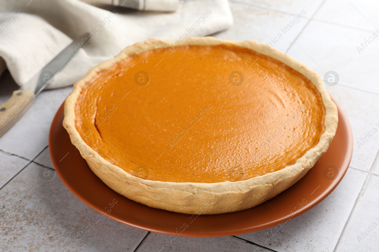 Photo of Tasty homemade pumpkin pie on light tiled table, closeup