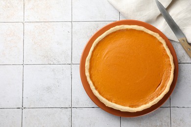 Tasty homemade pumpkin pie and knife on light tiled table, top view. Space for text