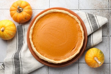 Tasty homemade pumpkin pie and fresh pumpkins on light tiled table, top view