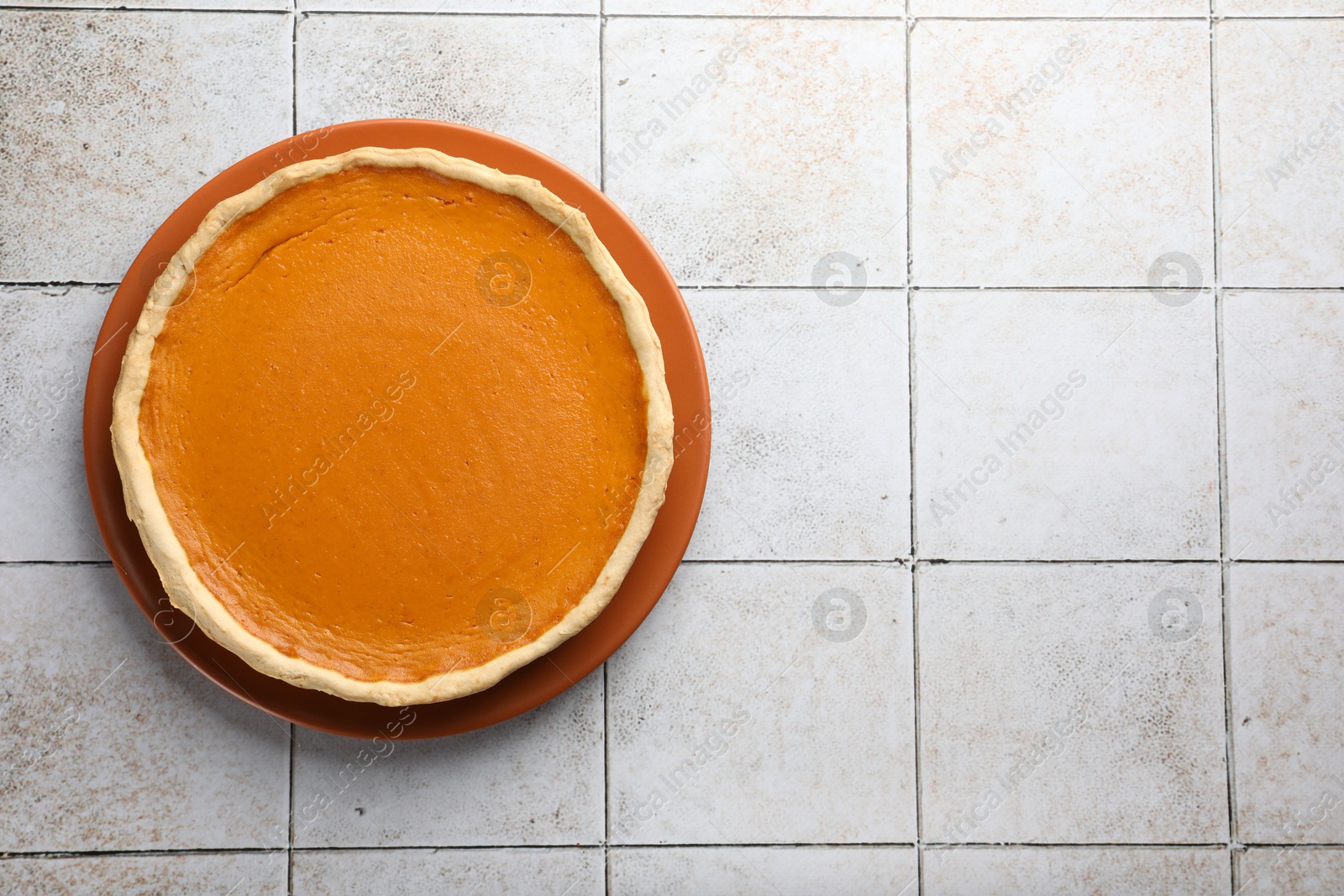 Photo of Tasty homemade pumpkin pie on light tiled table, top view. Space for text