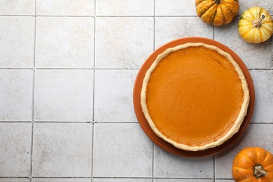 Tasty homemade pumpkin pie and fresh pumpkins on light tiled table, top view. Space for text