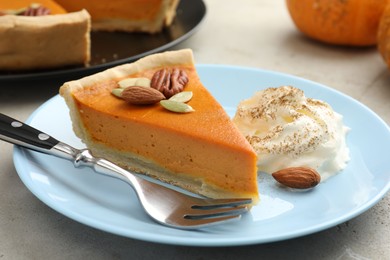 Photo of Piece of tasty homemade pumpkin pie with whipped cream, seeds and nuts on grey table, closeup