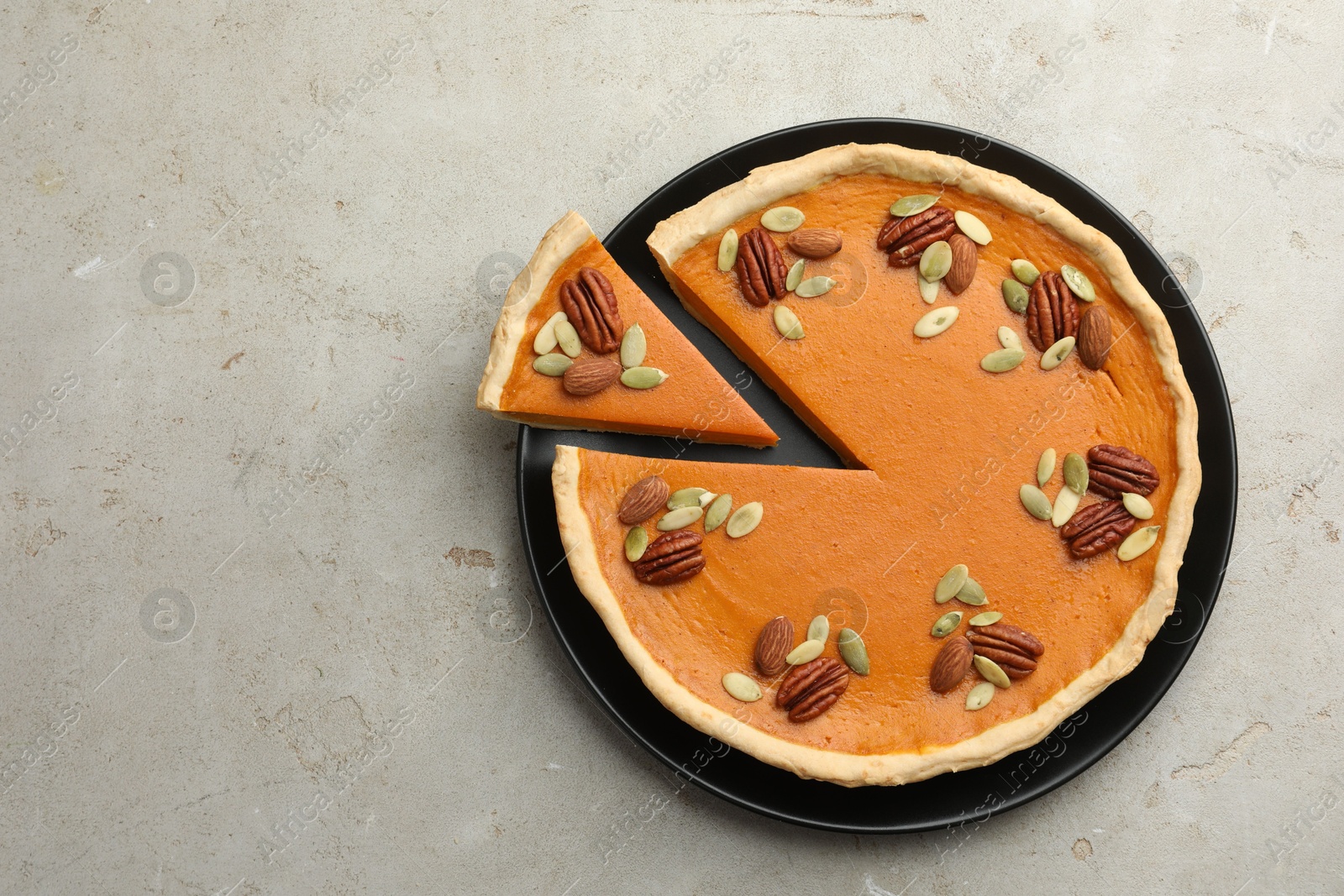 Photo of Tasty homemade pumpkin pie with seeds and nuts on grey table, top view. Space for text