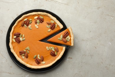 Tasty homemade pumpkin pie with seeds and nuts on grey table, top view. Space for text