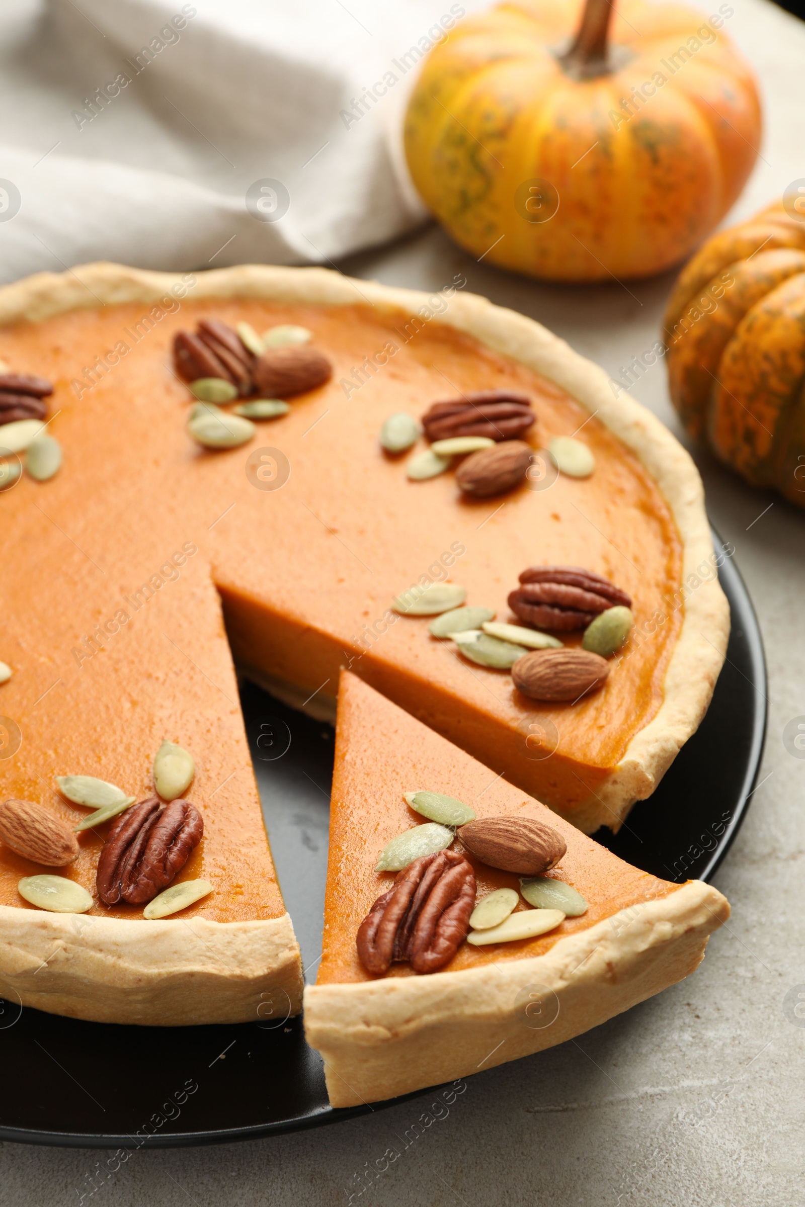 Photo of Tasty homemade pumpkin pie and fresh pumpkins on grey table, closeup