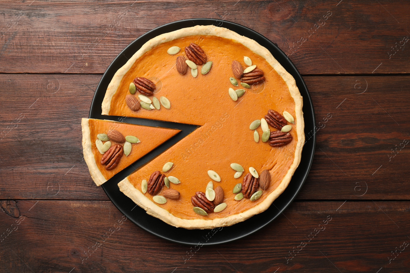 Photo of Tasty homemade pumpkin pie with seeds and nuts on wooden table, top view