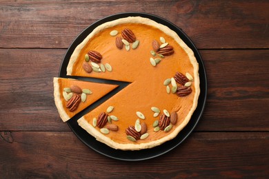 Tasty homemade pumpkin pie with seeds and nuts on wooden table, top view