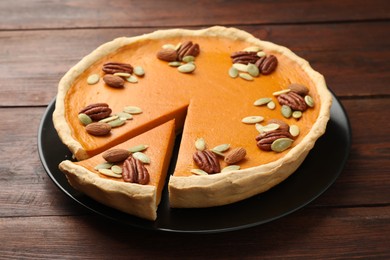 Photo of Tasty homemade pumpkin pie with seeds and nuts on wooden table, closeup