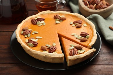 Photo of Tasty homemade pumpkin pie with seeds and nuts on wooden table, closeup