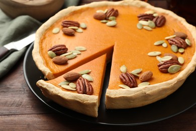 Tasty homemade pumpkin pie with seeds and nuts on wooden table, closeup