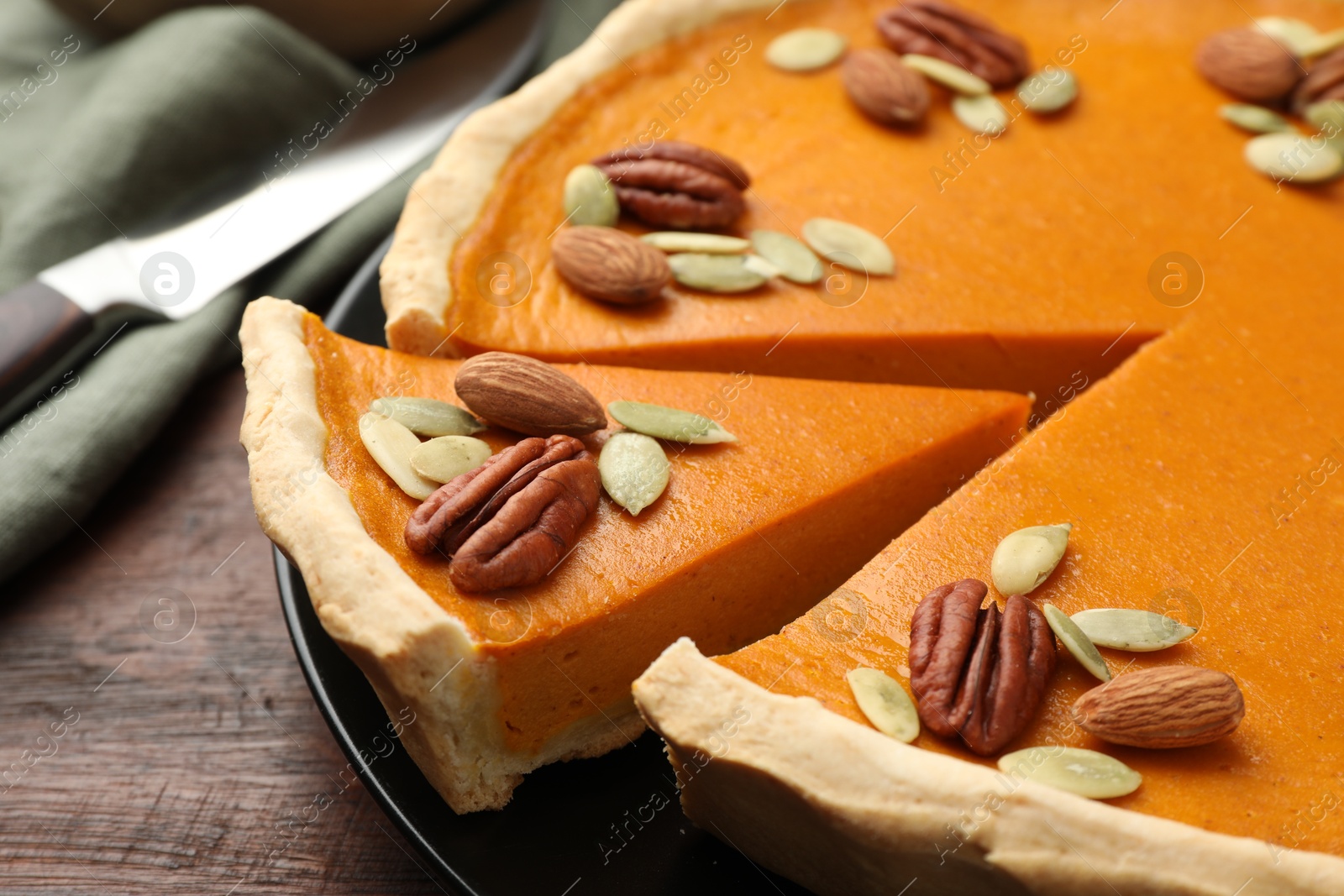 Photo of Tasty homemade pumpkin pie with seeds and nuts on wooden table, closeup