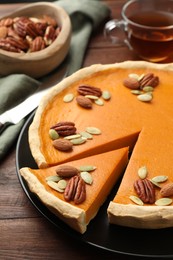 Photo of Tasty homemade pumpkin pie with seeds and nuts on wooden table, closeup