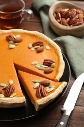 Photo of Tasty homemade pumpkin pie with seeds and nuts on wooden table, closeup