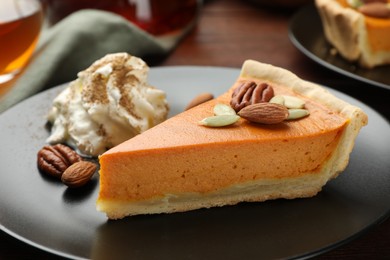 Photo of Piece of tasty homemade pumpkin pie with whipped cream, seeds and nuts on table, closeup