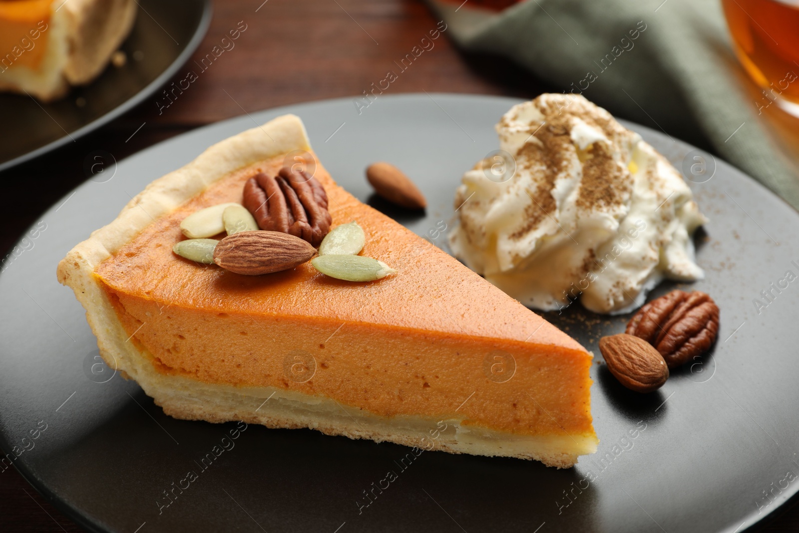 Photo of Piece of tasty homemade pumpkin pie with whipped cream, seeds and nuts on table, closeup